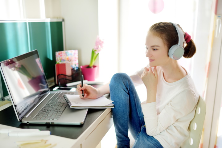 Jonge vrouw maakt aantekeningen achter laptop